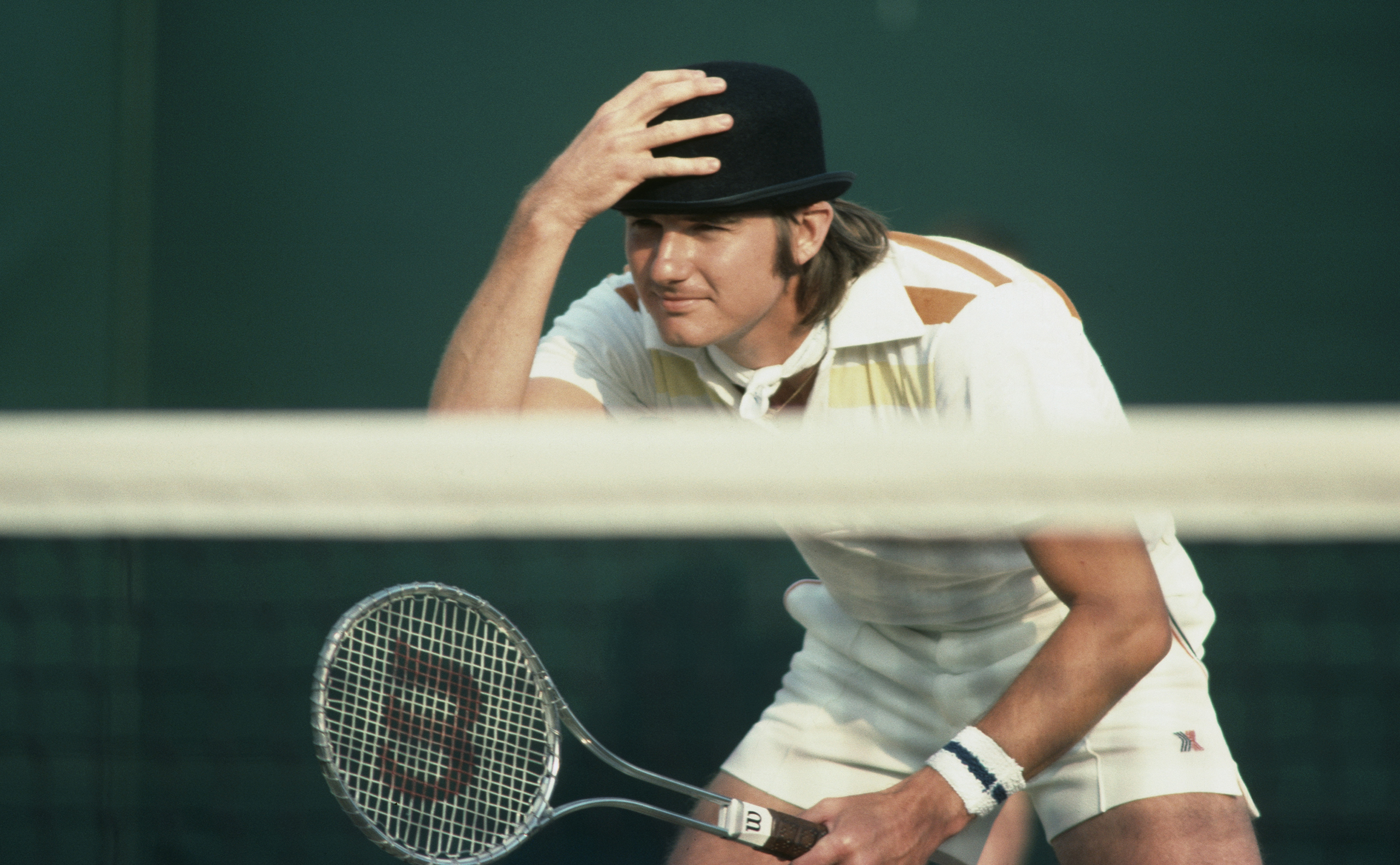 Jimmy Connors clowns and jokes with the spectators by wearing a bowler hat during a men's doubles match in 1976