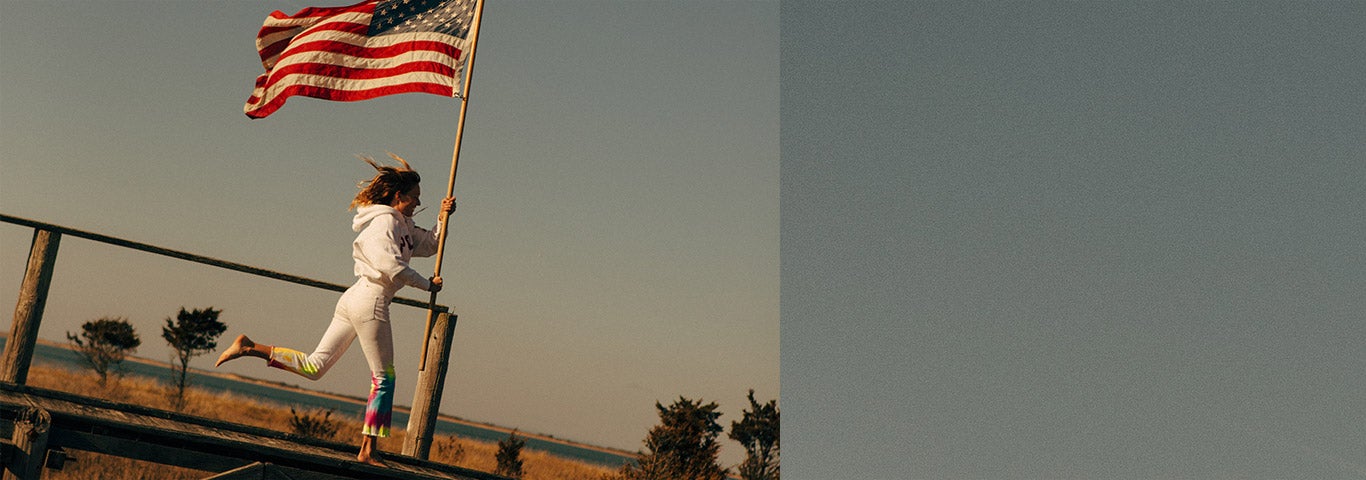 Woman in tie-dye white denim running and carrying American flag