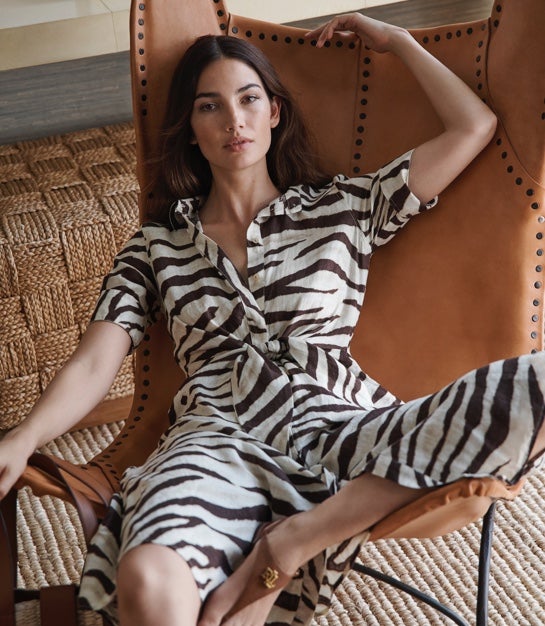 Model in chair wears zebra-print shirtdress and brown leather sandals.